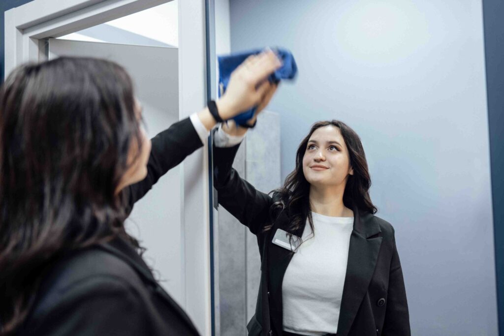 Young brunette woman in black jacket wipes window sill in fitnes